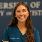 A smiling person in dental scrubs stands against a blurred background with text.