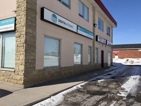 A dental clinic exterior on a clear day, with a stone facade and windows. Snow lines the path leading to the entrance.