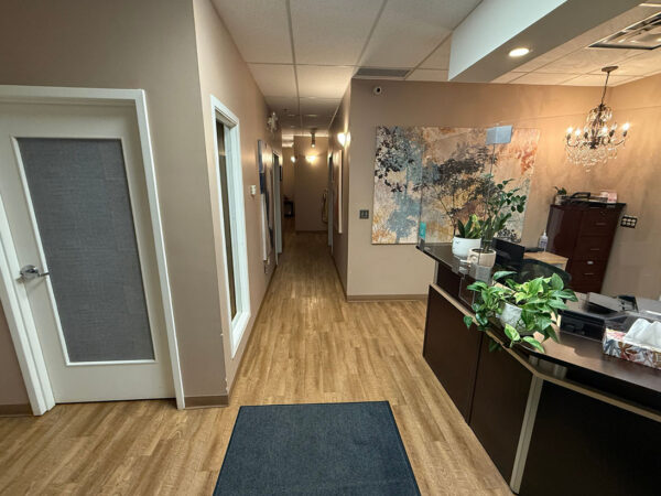 A dental office reception area with a counter and a hallway leading to treatment rooms. The decor includes plants and a large wall mural, creating a welcoming atmosphere.