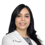 A woman with long dark hair is smiling confidently while wearing a white lab coat against a plain background.