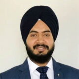 A man wearing a turban and a suit, smiling at the camera against a plain background.