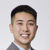 A person in a suit smiling at the camera against a plain background.