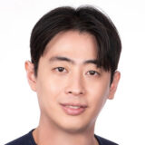 A person with short dark hair smiles at the camera against a plain white background.