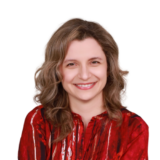 A person with wavy hair wearing a red patterned blouse smiles at the camera against a white background.