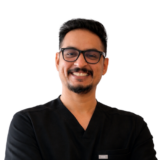 A smiling man with glasses, wearing a black shirt, stands with his arms crossed against a white background.