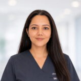 A smiling woman in a dental uniform stands in a bright, modern dental office, creating a welcoming and professional atmosphere.
