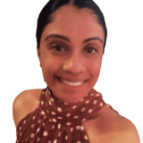 A person smiling warmly, wearing a brown polka dot sleeveless top, with a simple white background.