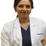 A smiling dentist in a white coat, seated and looking at the camera, creating a welcoming atmosphere.