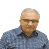 A person with glasses and grey hair is wearing a blue checked shirt, looking into the camera against a white background.