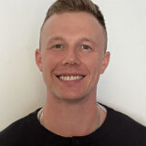 A person smiles warmly at the camera against a plain background, conveying friendliness and approachability.
