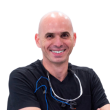 A smiling man in a black shirt with dental equipment around his neck, standing against a white background.