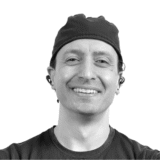 A person smiling warmly while wearing a cap and earrings, conveying a friendly and welcoming demeanor.