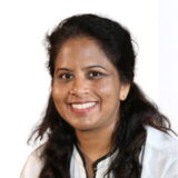 Smiling person with dark hair, wearing a white shirt, looking directly at the camera.