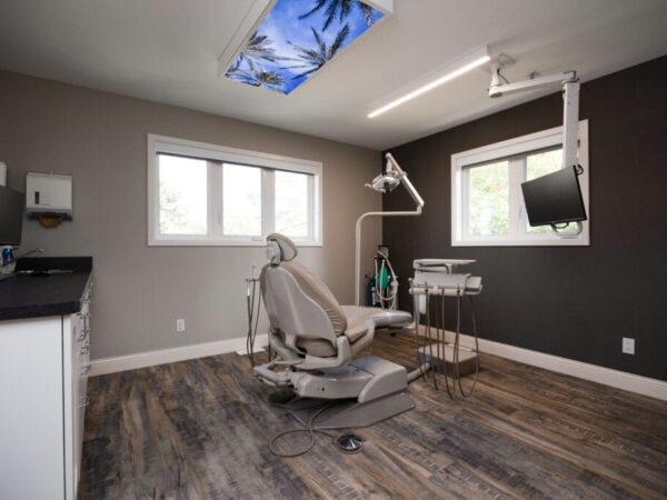 A modern dental office with a comfortable chair, overhead lights, and large windows bringing in natural light.