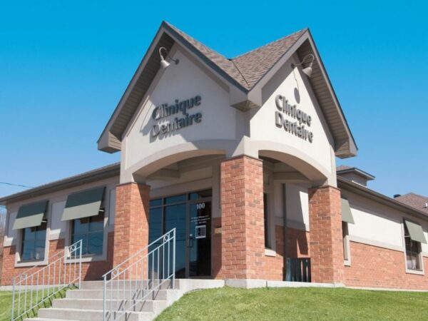 A modern dental clinic building with a brick and beige exterior under a clear blue sky.