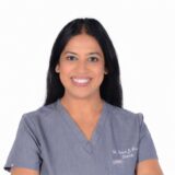 Smiling dentist in a grey uniform, standing confidently against a white background.