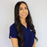 A smiling woman in navy scrubs stands against a plain background.