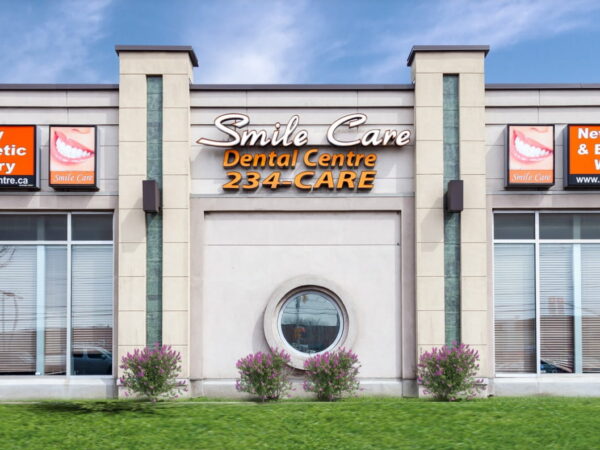 A dental clinic with a welcoming facade featuring large windows and signs for family, cosmetic, and emergency dentistry. Surrounded by neatly trimmed greenery, it conveys a friendly and professional atmosphere.